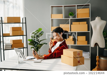 Startup small business SME, Entrepreneur owner African woman using smartphone or tablet taking receive and checking online purchase shopping order to preparing pack product box. in office Startup small business SME, Entrepreneur owner African woman using smartphone or tablet taking receive and checking online purchase shopping order to preparing pack product box. in office 102214644