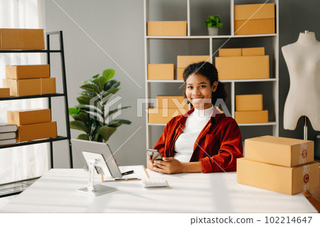 Startup small business SME, Entrepreneur owner African woman using smartphone or tablet taking receive and checking online purchase shopping order to preparing pack product box. in office Startup small business SME, Entrepreneur owner African woman using smartphone or tablet taking receive and checking online purchase shopping order to preparing pack product box. in office 102214647