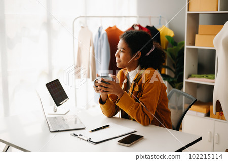 Calm curly brunette dark skinned woman on desk in office of fashion designer and holds tablet and smartphone. Calm curly brunette dark skinned woman on desk in office of fashion designer and holds tablet and smartphone. 102215114