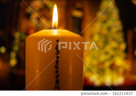 Candle with advent calendar on background of christmas tree lights decorations. Traditional Burning Christmas Wax Candles with numbers counting down for Christmas. Beautiful Advent At Home. Festive 102221837