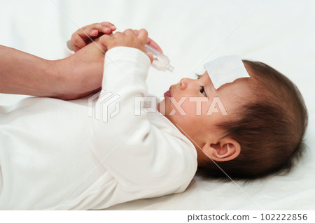 sick baby with cool fever pad gets nose drops by mother on bed 102222856