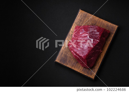 A piece of fresh raw beef with salt, spices and herbs on a wooden cutting board A piece of fresh raw beef with salt, spices and herbs on a wooden cutting board 102224686