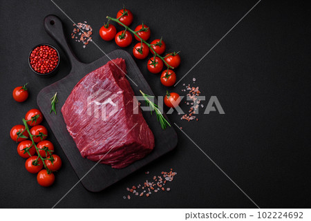 A piece of fresh raw beef with salt, spices and herbs on a wooden cutting board 102224692