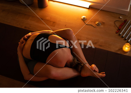 The girl is doing yoga in the studio with a dark warm light. The girl is doing yoga in the studio with a dark warm light. 102226341