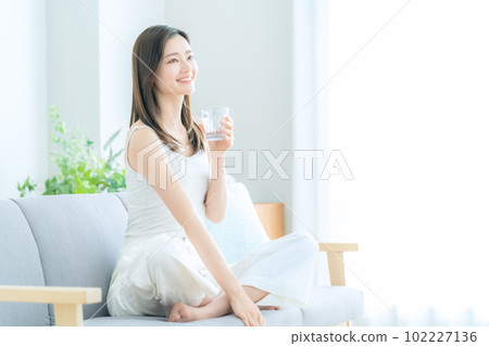 Young woman sitting on sofa in living room and drinking water 102227136