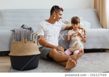 Full length portrait of smiling young adult man wearing white casual style T-shirt and jeans short sitting on floor with charming girl, playing with daughter during weekend. Full length portrait of smiling young adult man wearing white casual style T-shirt and jeans short sitting on floor with charming girl, playing with daughter during weekend. 102227589