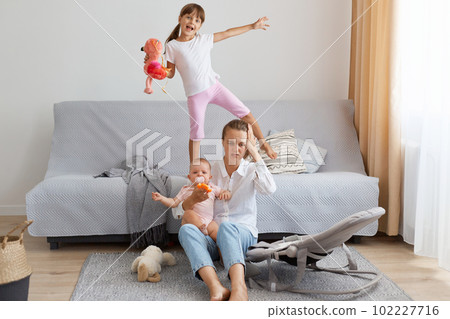 Indoor shot of mother in depression by screaming children, problems of motherhood, sitting on floor and suffering headache, don't know what to do with kids. 102227716
