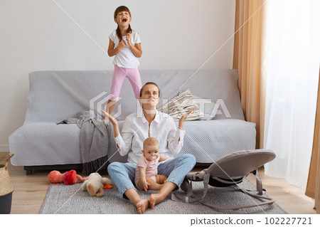 Horizontal shot of exhausted woman with dark hair sitting with crossed legs in casual attire and looking up with spread hands, being tired of noisy children. Horizontal shot of exhausted woman with dark hair sitting with crossed legs in casual attire and looking up with spread hands, being tired of noisy children. 102227721