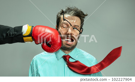Mature man, businessman in red tie getting boxing punch in jaw from business competitors over grey background. Concept financial loses, business fall, deadlines, economic crisis Mature man, businessman in red tie getting boxing punch in jaw from business competitors over grey background. Concept financial loses, business fall, deadlines, economic crisis 102227904
