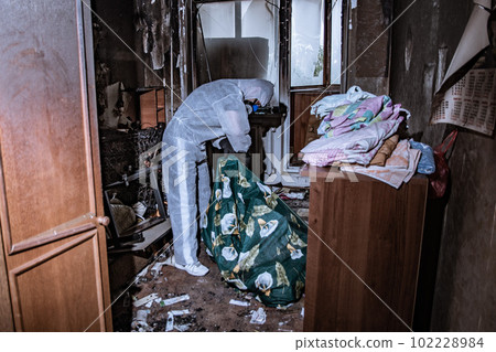 a specialist in a protective suit from a cleaning company cleans a destroyed housing after a fire a specialist in a protective suit from a cleaning company cleans a destroyed housing after a fire 102228984