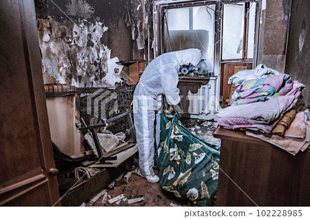 a specialist in a protective suit from a cleaning company cleans a destroyed housing after a fire 102228985