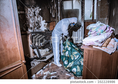 a specialist in a protective suit from a cleaning company cleans a destroyed housing after a fire 102228986