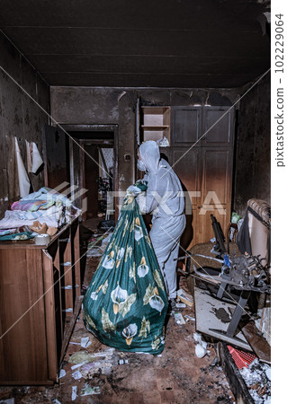 a specialist in a protective suit from a cleaning company cleans a destroyed housing after a fire 102229064