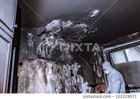 a specialist in a protective suit from a cleaning company cleans a destroyed housing after a fire 102229071