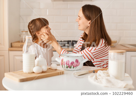 Portrait of Caucasian young adult woman and her little female child playing while baking in kitchen at home, expressing positive emotions and happiness. 102229460