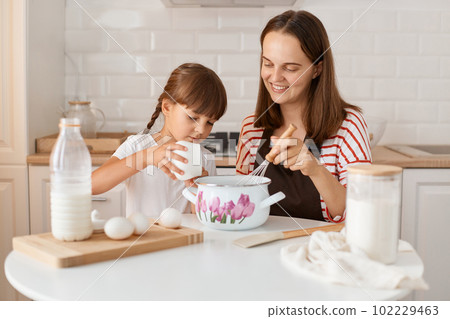 Attractive satisfied young mother and her little daughter baking in kitchen at home, preparing homemade pastry together, expressing happiness, female kid ad sugar. Attractive satisfied young mother and her little daughter baking in kitchen at home, preparing homemade pastry together, expressing happiness, female kid ad sugar. 102229463