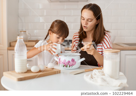 Indoor shot of concentrated mother and her cute little daughter baking at home, mommy teaching her child to do bake pastry or cookie, spending time together. Indoor shot of concentrated mother and her cute little daughter baking at home, mommy teaching her child to do bake pastry or cookie, spending time together. 102229464