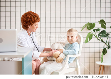 Pediatrician listening to breathing in the lungs and heartbeat with stethoscope. Portrait of adorable little boy visiting doctor. Pediatrician listening to breathing in the lungs and heartbeat with stethoscope. Portrait of adorable little boy visiting doctor. 102230361