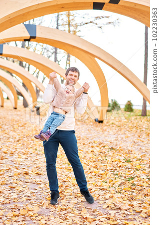 Portraits of a cute 1 year old baby girl and her young father. Walking in Yellow Autumn Park. Leaf fall and yellow leaves. sunny day Portraits of a cute 1 year old baby girl and her young father. Walking in Yellow Autumn Park. Leaf fall and yellow leaves. sunny day 102230363