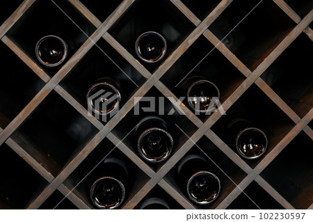 Elite dark glass wine bottles stacked on wooden racks in cellar, market, restaurant or home. Collection of bottles wine at shelf Elite dark glass wine bottles stacked on wooden racks in cellar, market, restaurant or home. Collection of bottles wine at shelf 102230597