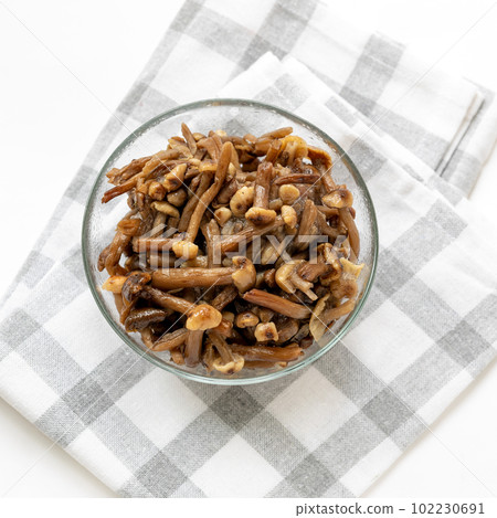 Glass bowl full of frozen wild forest mushrooms honey agarics on checkered napkin on white. Top view 102230691