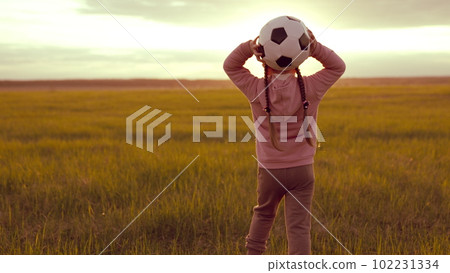 Chil runs across green field kicking ball sunset. Silhouette Child playing ball. love football. children's football game. running feet green lawn summer. wheat. kids running concept. girl daughter 102231334