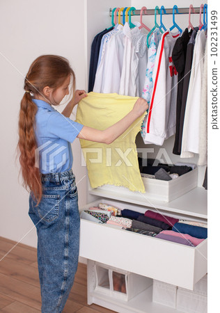A ten-year-old Girl puts a t-shirt in a drawer. 102231499
