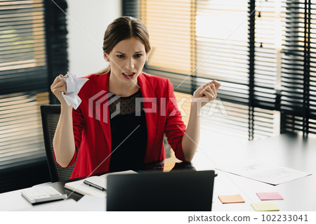 Furious caucasian businesswoman sitting at desk and crumpling paper, having problem with project Furious caucasian businesswoman sitting at desk and crumpling paper, having problem with project 102233041