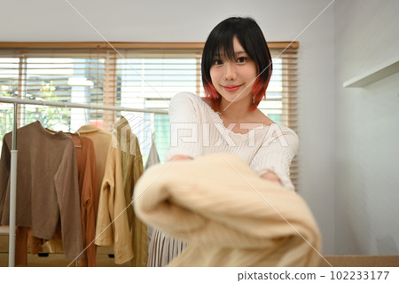 Headshot of young woman showing clothes in front of smartphone camera, selling clothes online by streaming 102233177