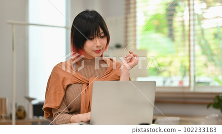 Charming young asian woman in stylish clothes working on laptop computer at modern home office Charming young asian woman in stylish clothes working on laptop computer at modern home office 102233183