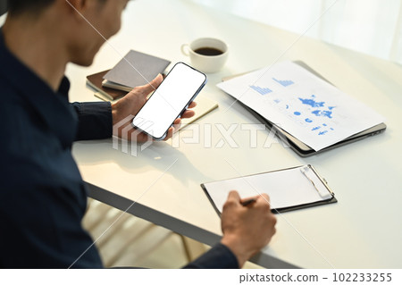 Male employee sitting at working desk and using smartphone. Blank screen for graphic display montage Male employee sitting at working desk and using smartphone. Blank screen for graphic display montage 102233255