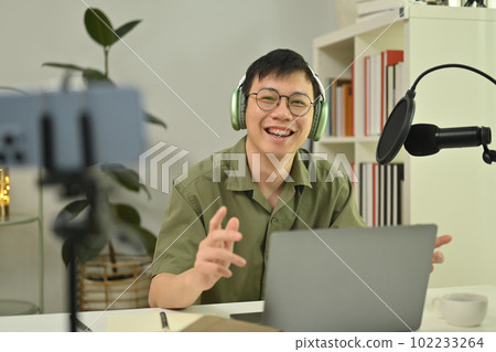 Cheerful male radio host using microphone and laptop to recording podcast in home studio. Radio, podcasts and technology concept 102233264