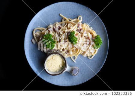 Pasta carbonara with bacon on blue plate isolated on black background side view  102233356