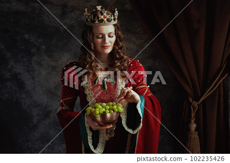 happy medieval queen in red dress with plate of grapes 102235426
