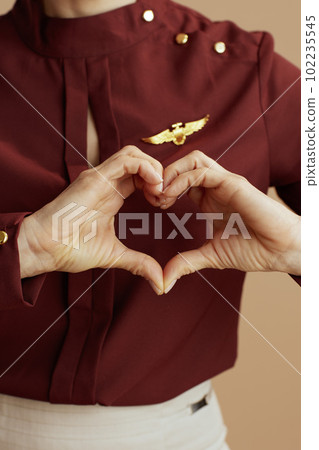 Stylish female air hostess showing heart hands against beige 102235545
