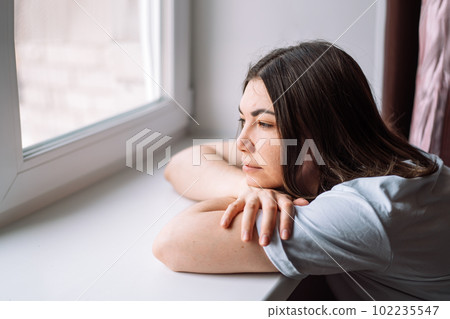 Lady lay down on the windowsill and looks out the window 102235547