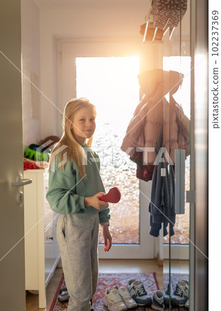 Cute serious 10 year little school girl child comb long blond hair with hairbrush near mirror against bright sun light in window at sunrise morning. Preteen independent kid prepare self go to school 102237369