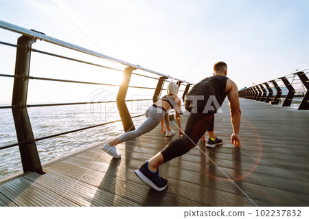 Romantic couple doing sport together at the beach pier. Two sporty athletes doing warming-up excersises. 102237832