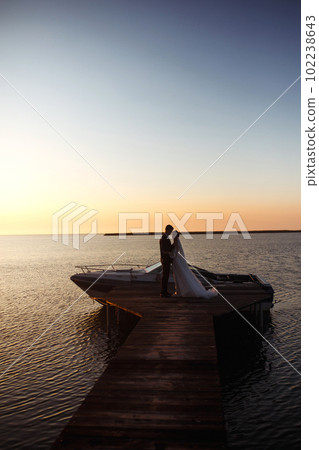 Beautiful bride and stylish groom together on the bridge against the background of the boat at sunset. 102238643