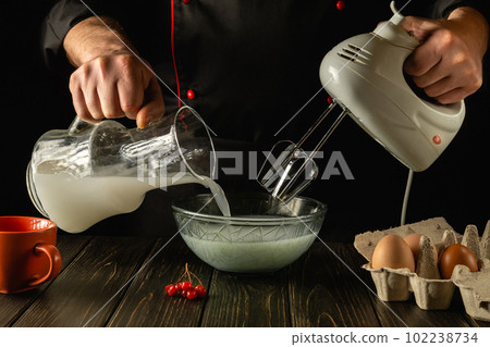 Professional chef prepares a delicious breakfast with milk and eggs in the kitchen using an electric hand mixer. The cook pours the poloko into a deep plate. Delicious recipe menu for hotel. 102238734