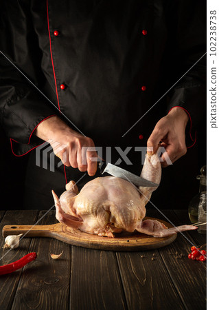 Professional chef cuts raw chicken with a knife in the kitchen. Cooking chicken for lunch. Grande cuisine. Professional chef cuts raw chicken with a knife in the kitchen. Cooking chicken for lunch. Grande cuisine. 102238738