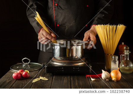 Cook prepares Italian pasta in a saucepan with vegetables. Close-up of chef hands while cooking in restaurant kitchen. European cuisine Cook prepares Italian pasta in a saucepan with vegetables. Close-up of chef hands while cooking in restaurant kitchen. European cuisine 102238740