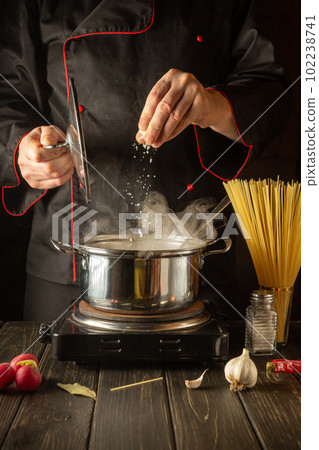 Cooking Italian spaghetti in the kitchen. The chef adds salt to Stock pot of boiling water. Grande cuisine. Cooking Italian spaghetti in the kitchen. The chef adds salt to Stock pot of boiling water. Grande cuisine. 102238741