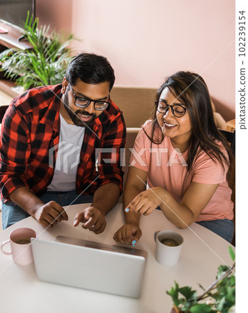 Latino or indian man and woman couple use their laptop in the living room to make video calls. Video call and online chat with family 102239154