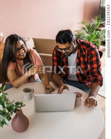 Happy indian family couple cuddle at desk make video call to friends using laptop webcam. Loving young spouses look at computer screen waving hands in good mood greeting parents communicating online 102239163