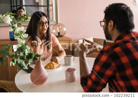 Happy couple eating breakfast and talking at dining table in morning. Indian girl and latino guy. Relationship and diversity concept 102239211