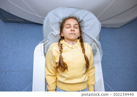 Little girl keeps eyes closed moving into mri scan machine before undergoing medical examination. 102239440