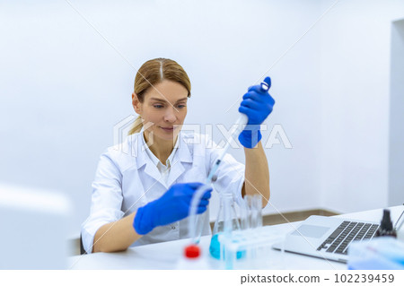 Female scientist in protective gloves dropping liquid substance into the test tube with a pipette Female scientist in protective gloves dropping liquid substance into the test tube with a pipette 102239459