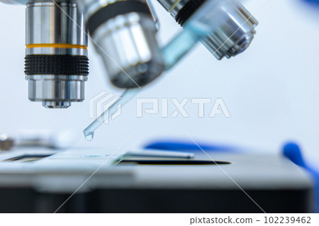 Unknown scientist dropping liquid from dropper to petri dish on microscope. Unknown scientist dropping liquid from dropper to petri dish on microscope. 102239462