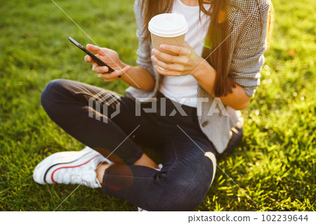 The girl holds the phone and coffee in hand. Sunset. Summertime. 102239644